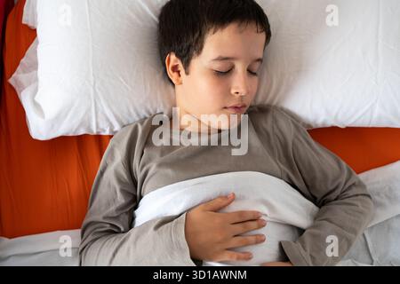 Dall'alto del raccolto anonimo maschio in pigiama sdraiato a letto sotto coperta calda e dormire in camera da letto Foto Stock