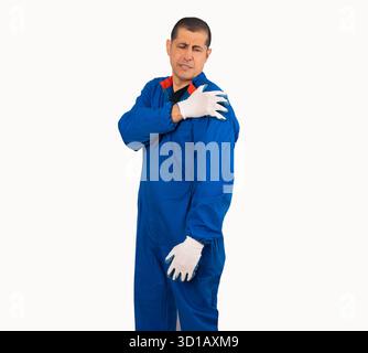Meccanico ispanico che si tocca la spalla indossando tute blu su sfondo bianco isolato Foto Stock