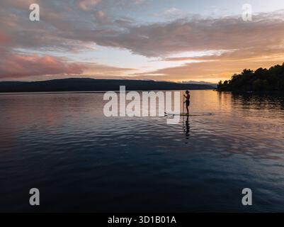 Vista aerea di un solitario paddleboarder scivola attraverso le acque tranquille mentre il sole dipinge il cielo con tonalità ardenti, l'isola di Moso, la provincia di Shefa, Vanuatu. Foto Stock