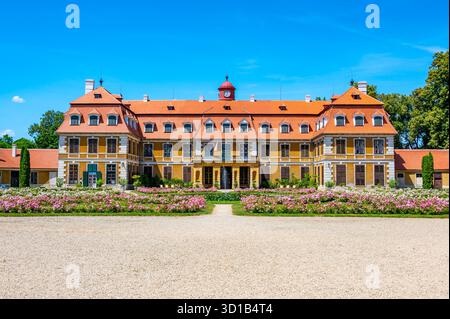 Vista panoramica del castello di Rajec Jestrebi in una soleggiata giornata estiva con cielo blu, rose rosa fiorenti e una fontana di fronte all'edificio storico. Foto Stock
