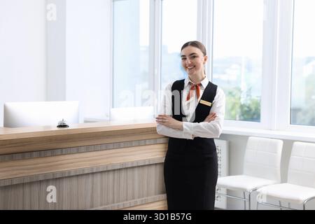 Il receptionist è felice in uniforme vicino al banco della reception all'interno Foto Stock