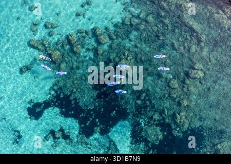 Vista aerea dei paddle board che galleggiano nelle acque cristalline turchesi, creando un contrasto sorprendente con il fondale roccioso scuro, Illes Balears, Spagna. Foto Stock