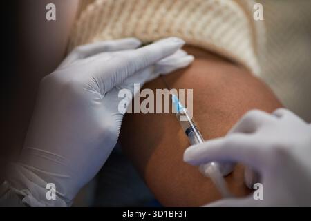Paziente nero che riceve la vaccinazione nella parte superiore del braccio con guanti di assistenza sanitaria che somministra l'iniezione utilizzando siringa, primo piano su mani e braccio, procedura medica in corso Foto Stock