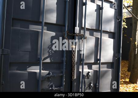 Due porte pesanti sono chiuse a chiave con una catena, circondate da un vivace fogliame autunnale. Foto Stock
