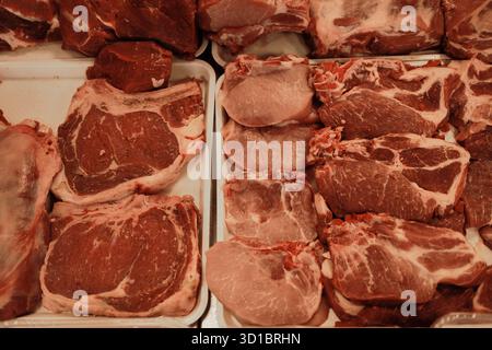 Vari tagli di manzo crudo ordinati in un'esposizione di macelleria. Fondo di carne rossa fresca per piatti e temi culinari. Foto Stock