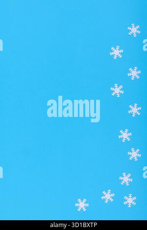 Sfondo invernale minimalista con fiocchi di neve di carta bianca disposti su una superficie blu brillante Foto Stock