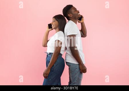 Una coppia allegra si diverte a conversare sugli smartphone con sfondo rosa Foto Stock