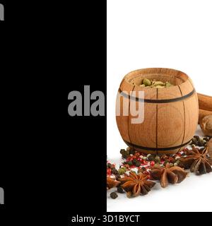 Una piccola botte di legno riempita di cialde verdi di cardamomo sorge tra un mucchio di anice stellato, grani di pepe e noce moscata, isolata Foto Stock