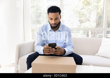 Uomo che usa lo smartphone seduto sul divano con il pacco Foto Stock