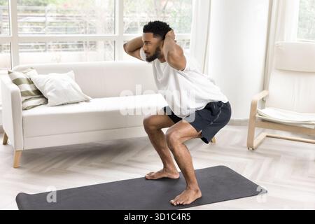 Giovane che esegue squat con le mani dietro la testa Foto Stock