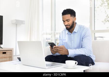 Uomo concentrato che usa lo smartphone seduto sul divano Foto Stock