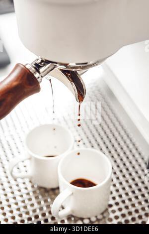 Caffè estratto gocciolando da una macchina da caffè professionale in tazze bianche durante un rituale del caffè mattutino Foto Stock