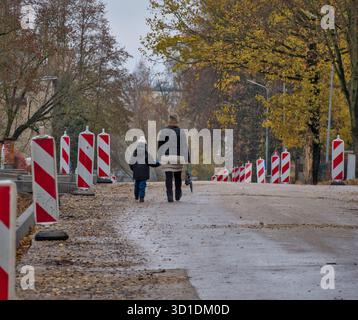 Madre e bambino camminano oltre le barriere stradali in una strada in autunno Foto Stock