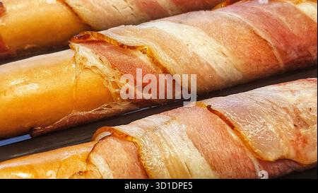Primo piano di succose salsicce avvolte in pancetta di hot dog su un vassoio da forno Foto Stock