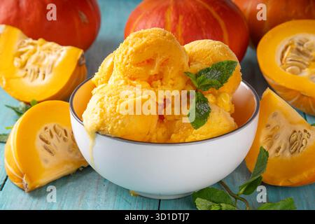 Ciotola per gelato alla zucca. Gustoso gelato con zucca in una ciotola in porzioni, su un tavolo di legno con zucca a fette, spazio per copiare Foto Stock