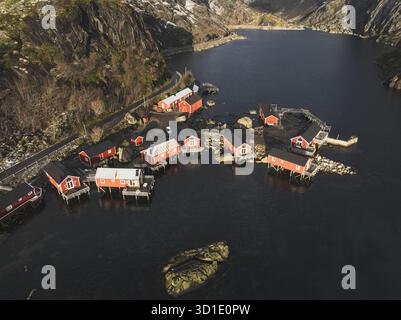 Veduta aerea delle vivaci cabine rosse raggruppate su palafitte sulle acque tranquille e scure, incorniciate da aspre montagne spolverate di neve, Reine, Nordland, Norvegia Foto Stock