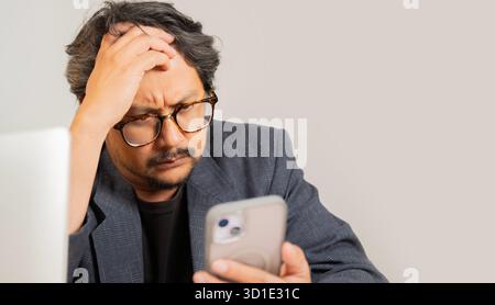 Uomo d'affari maturo che utilizza lo smartphone e stressato con la mano sulla testa, scioccato dalla vergogna e dal volto a sorpresa. Paura e turbata per errore. Foto Stock