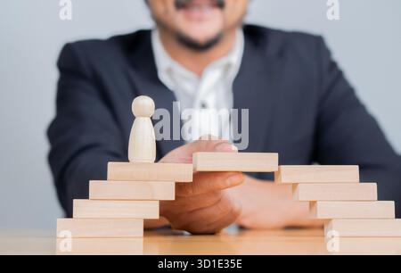 Uomo che risolve i problemi costruendo un ponte con blocchi di legno per coprire un vuoto per le piccole persone icona di legno che camminano attraverso. Foto Stock