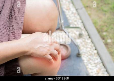 Colpo ad angolo alto di una donna anziana tiene il ginocchio affetto da dolore alle articolazioni del ginocchio con bastone da passeggio. Concetto senior di salute. Foto Stock