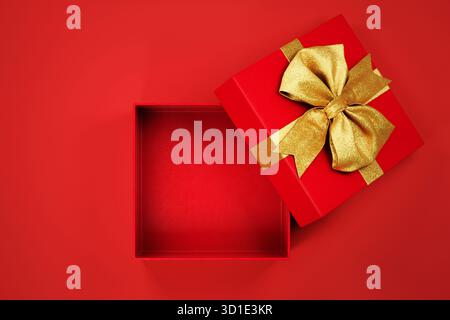 Apri la confezione regalo di natale con il fiocco dorato aperto su sfondo rosso. Regalo di Capodanno con modello mockup a nastro dorato. Foto Stock