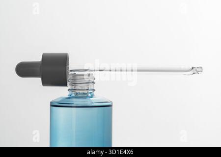 Contagocce lungo in vetro appoggiato su flaconi in vetro blu su sfondo bianco retroilluminato. Concetto di cosmetica, cura della pelle, siero, dettaglio del prodotto, minimalismo, Foto Stock