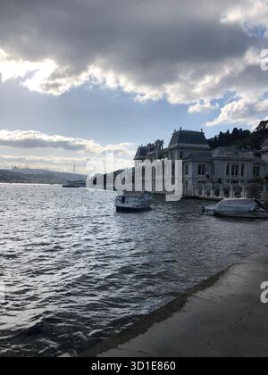 Eleganti ville sul lungomare lungo il Bosforo a Istanbul, Turchia, sotto un cielo spettacolare con barche che riposano su acque calme. Foto Stock