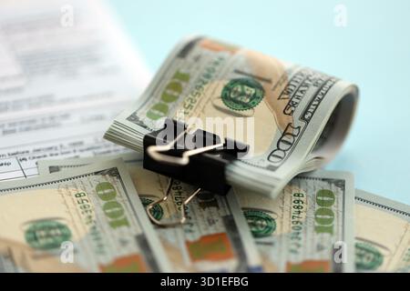 Grande quantità di banconote in dollari statunitensi sul tavolo con modulo di dichiarazione dei redditi individuale da vicino. Concetto di tassazione e contabilità negli Stati Uniti Foto Stock
