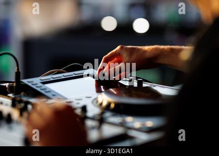 Mano di un DJ che regola le manopole su una console di mixaggio audio durante un'esibizione dal vivo sotto una luce soffusa. Foto Stock