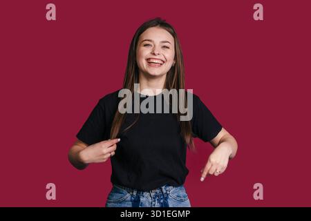 Giovane donna sorridente che punta su una t-shirt nera, ambasciatrice del marchio Foto Stock