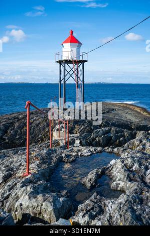 Kvalen fyr, un faro rosso e bianco si erge su un terreno roccioso vicino al mare, con un sentiero che conduce ad esso, tiro verticale, Haugesund, Norvegia Foto Stock
