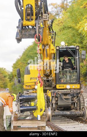 Primo piano di un escavatore con un operaio, ambiente autunnale su binari ferroviari, segnaletica di costruzione sulla Hermann Hessebahn, Calw, Germania Foto Stock