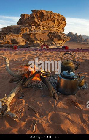Due teiere accanto a un fuoco aperto nella sabbia del deserto, rocce erose sullo sfondo, Wadi Rum, Giordania Foto Stock