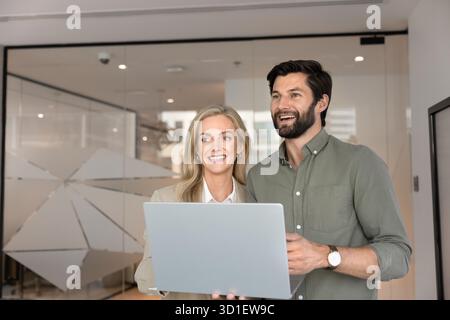 Un paio di colleghi felici che tengono un portatile, in piedi insieme Foto Stock