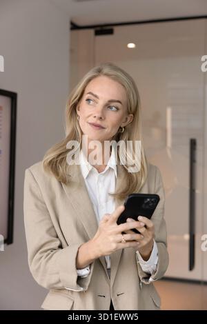 Giovane donna professionale attenta e positiva che pensa alla comunicazione telefonica Foto Stock