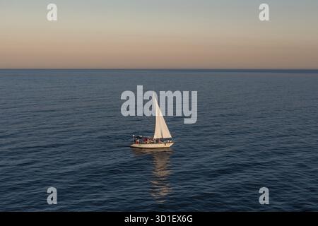 Barca a vela solitaria che galleggia sulle calme acque dell'oceano durante un tramonto sereno Foto Stock
