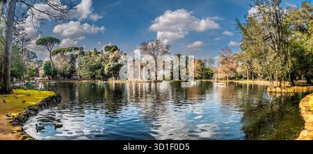 Un tranquillo parco caratterizzato da un padiglione decorativo del tempio su un'isola in un tranquillo lago, circondato da alberi e un cielo blu. Perfetto per la natura, trav Foto Stock
