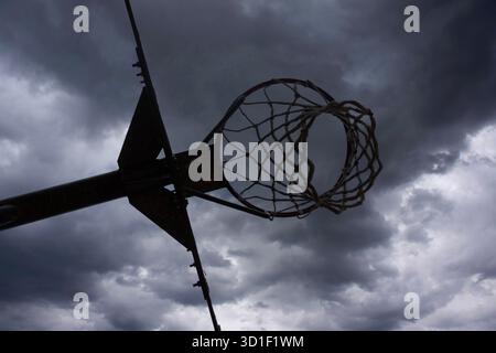 Canestro da basket contro il cielo nuvoloso scuro, simboleggiando il tempo tempestoso e gli sport all'aperto Foto Stock