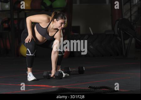 Atleta donna incinta che fa un singolo sumo deadlift high pull con il manubrio Foto Stock