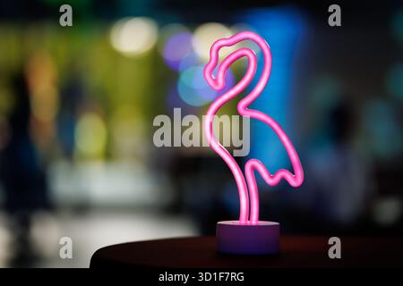 Lampada fenicottero al neon rosa stilizzata che si illumina su un tavolo con luci di sfondo colorate sfocate. Foto Stock