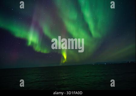 Un'esposizione mozzafiato dell'aurora boreale illumina il cielo notturno su un vasto oceano, creando uno spettacolo affascinante di sfumature verdi e viola Foto Stock