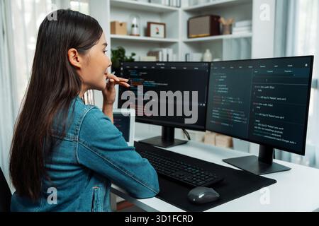 Giovane sviluppatore di IT asiatico che cerca informazioni online su pc per una bella posa con i dati del programma di codifica dell'applicazione del sito web, indossando una camicia di jeans Foto Stock