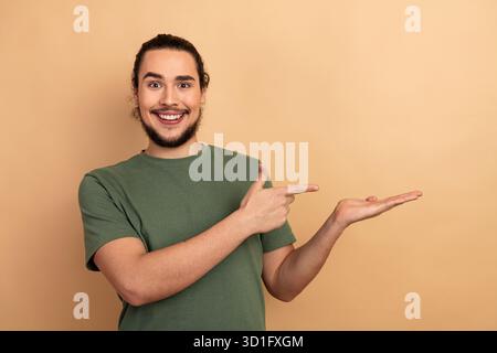 Giovane felice in camicia verde che presenta su sfondo beige Foto Stock