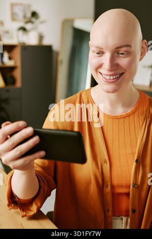 Ritratto di una giovane donna che sorride mentre utilizza lo smartphone in interni Foto Stock