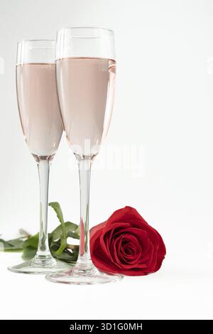 Due bicchieri di champagne e una rosa rossa isolata su sfondo bianco Foto Stock