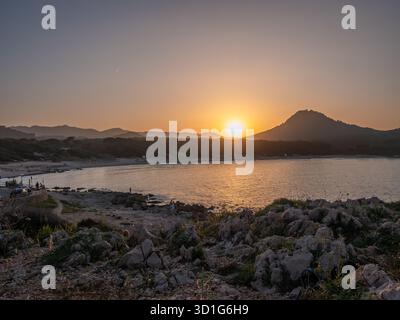 Un tramonto sereno a Cala Rajada, un calmo specchio d'acqua di Maiorca con una montagna lontana e una costa rocciosa, bagnata dalla calda luce dorata, Cala Ratjada, ma Foto Stock