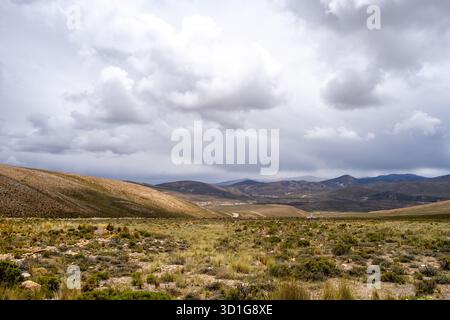 Una vasta e arida valle sotto un cielo spettacolare in Perù, che mostra la bellezza naturale del deserto e le montagne circostanti. Foto Stock