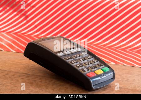 Terminale POS su tavolo in legno con sfondo a righe rosse e bianche, concetto di vendita al dettaglio Foto Stock