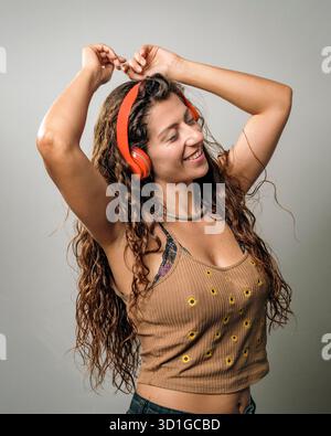 Una giovane donna sta ballando felicemente, indossando cuffie luminose. I suoi movimenti vivaci riflettono il suo amore per la musica e la luce calda la mette in risalto Foto Stock