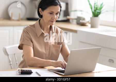 Contabile donna anziana impegnata che utilizza la calcolatrice del notebook presso l'ufficio domestico Foto Stock