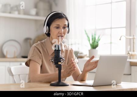 Donna anziana che indossa le cuffie che parla in video utilizzando il microfono del notebook Foto Stock